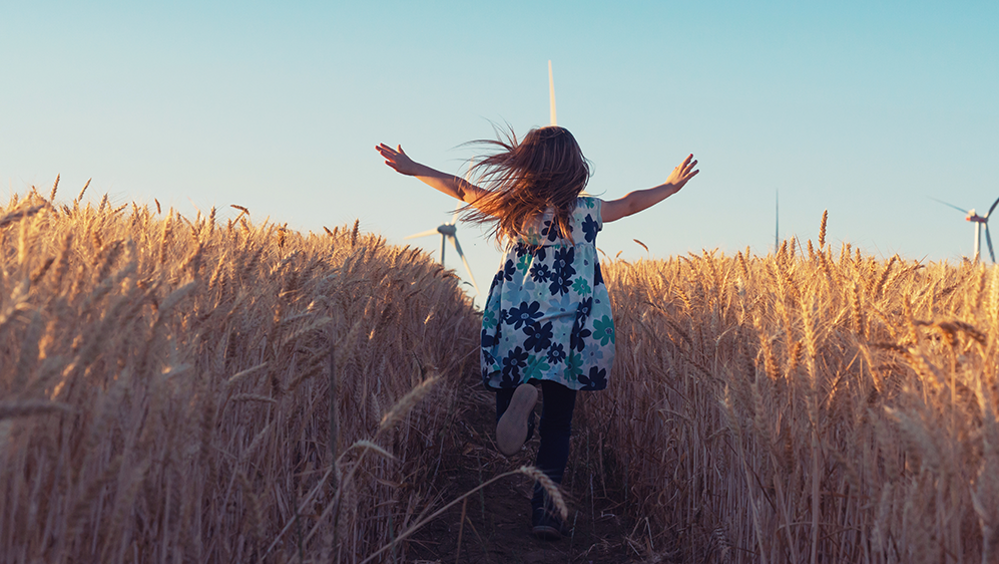 Bambina che corre in un campo di grano con pale eoliche sullo sfondo