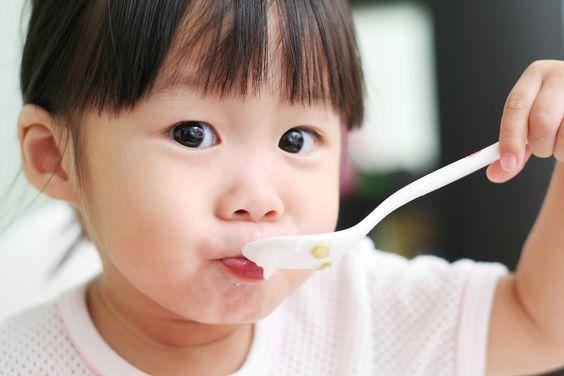 Una bambina che mangia un cucchiaio di cibo