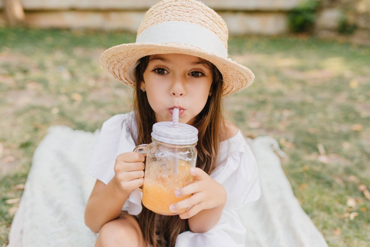 Bambina con cappello di paglia beve frullato di frutta da bicchiere di vetro