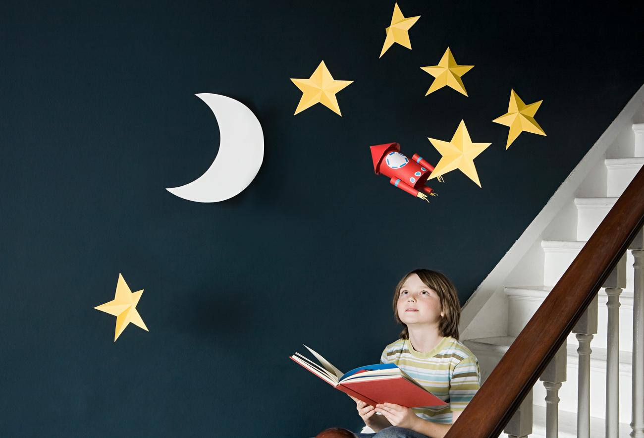 Bambino che legge un libro con sullo sfondo le stelle e la luna