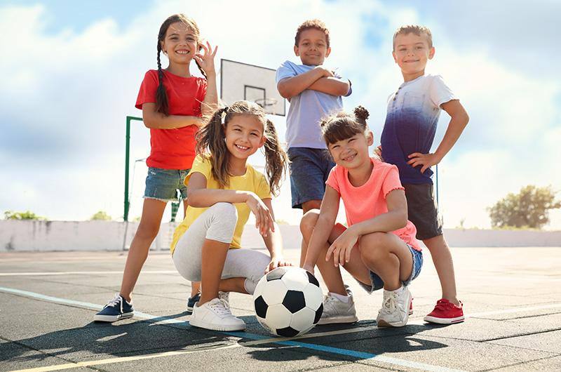 Bambini sorridenti con un pallone da calcio su un campetto da basket