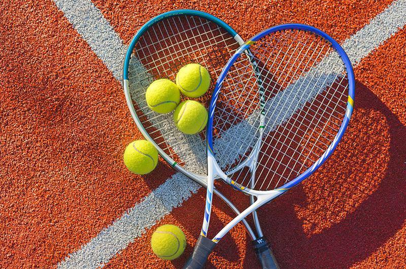 Due racchette da tennis appoggiate con cinque palline su un campo da tennis