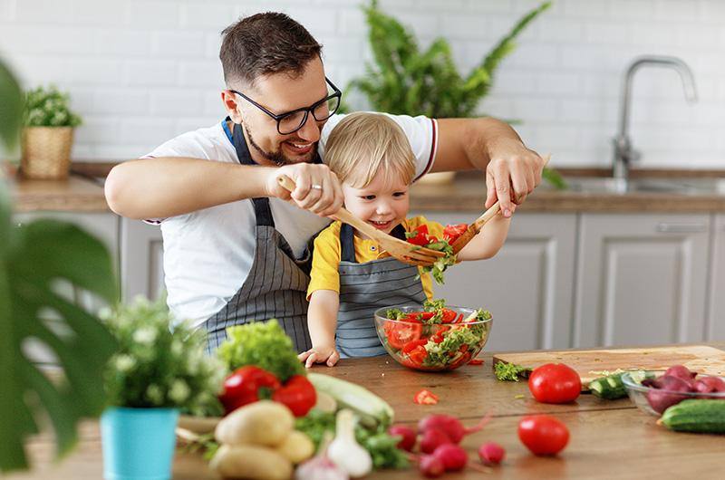 Papà e figlio piccolo sorridenti mentre preparano una insalata di verdure miste