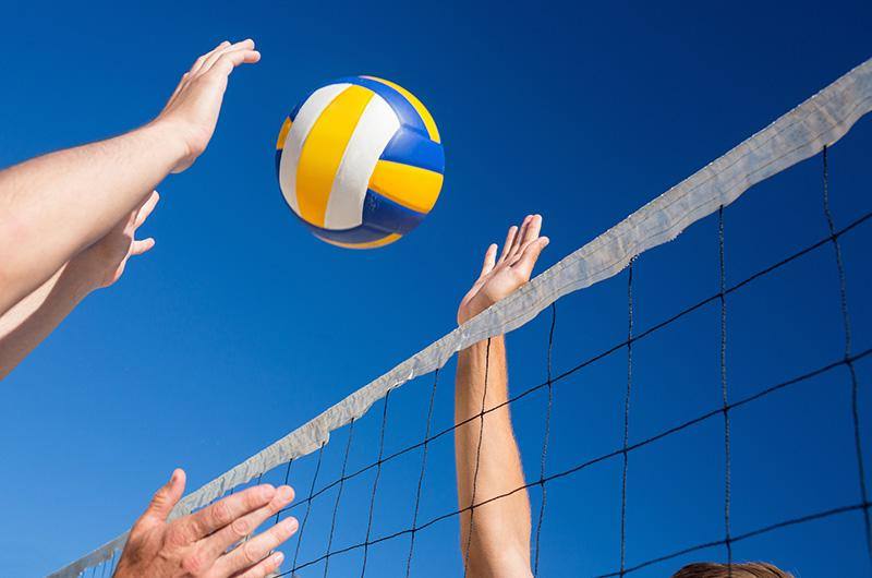Pallone da volley sopra una rete con due persone che tentano di schiacciare la palla