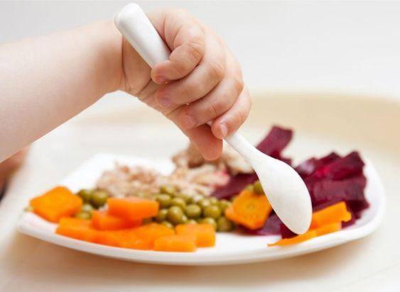 La mano di un bimbo intenzionato a mangiare il suo piatto di piselli, carote, barbabietole e pollo
