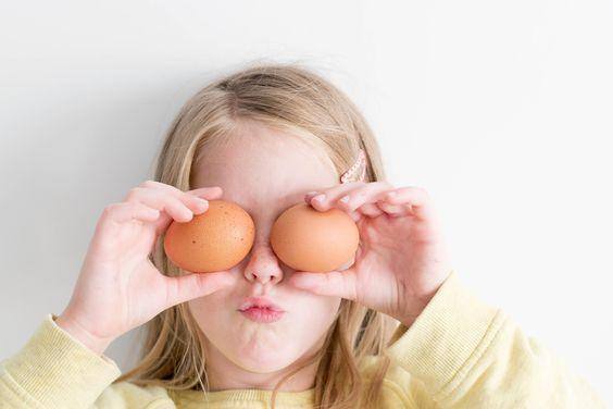 Una bambina che tiene due uova davanti agli occhi
