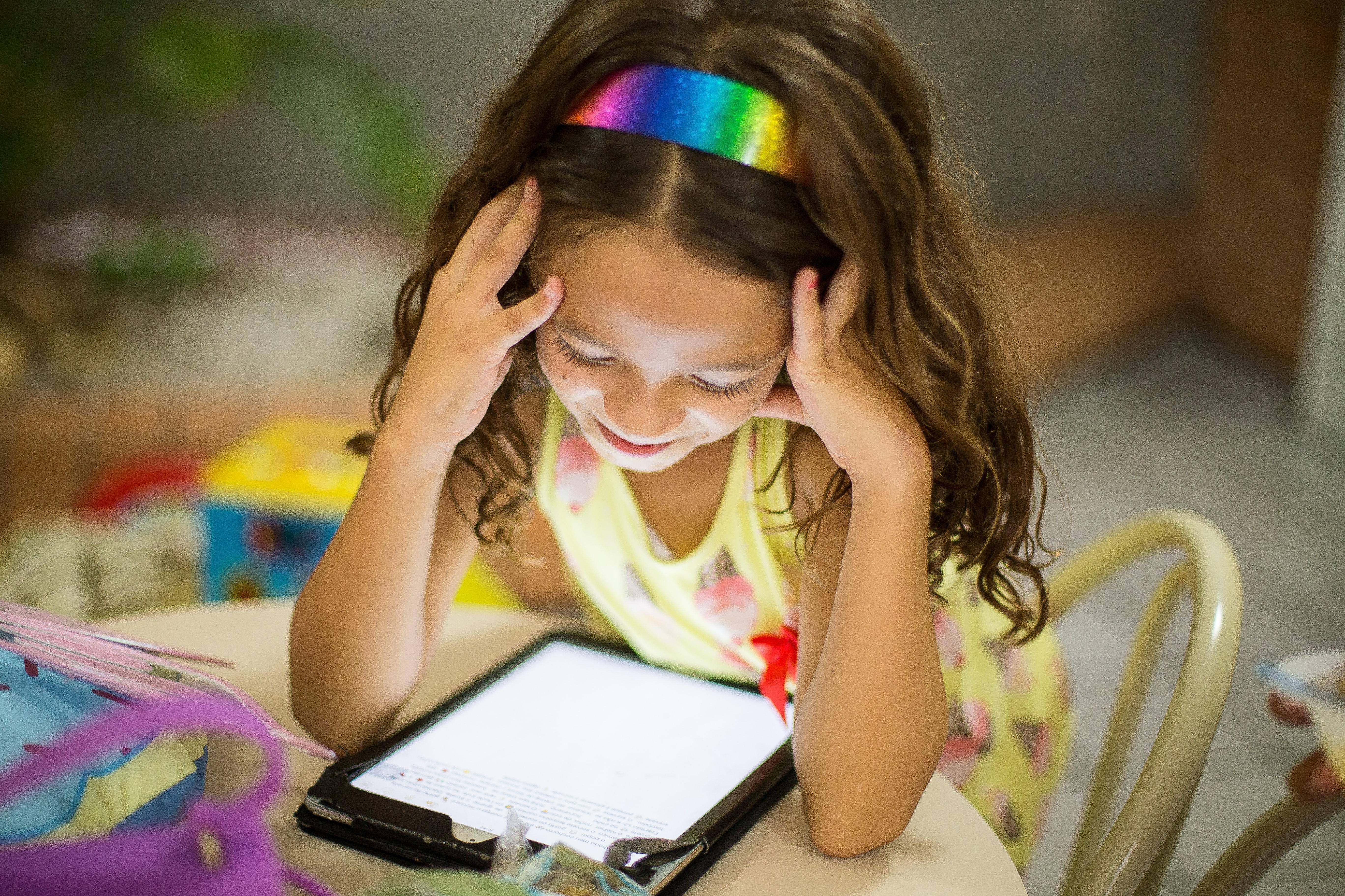 Bambina con capelli lunghi e frontino arcobaleno legge e-book nella sua cameretta