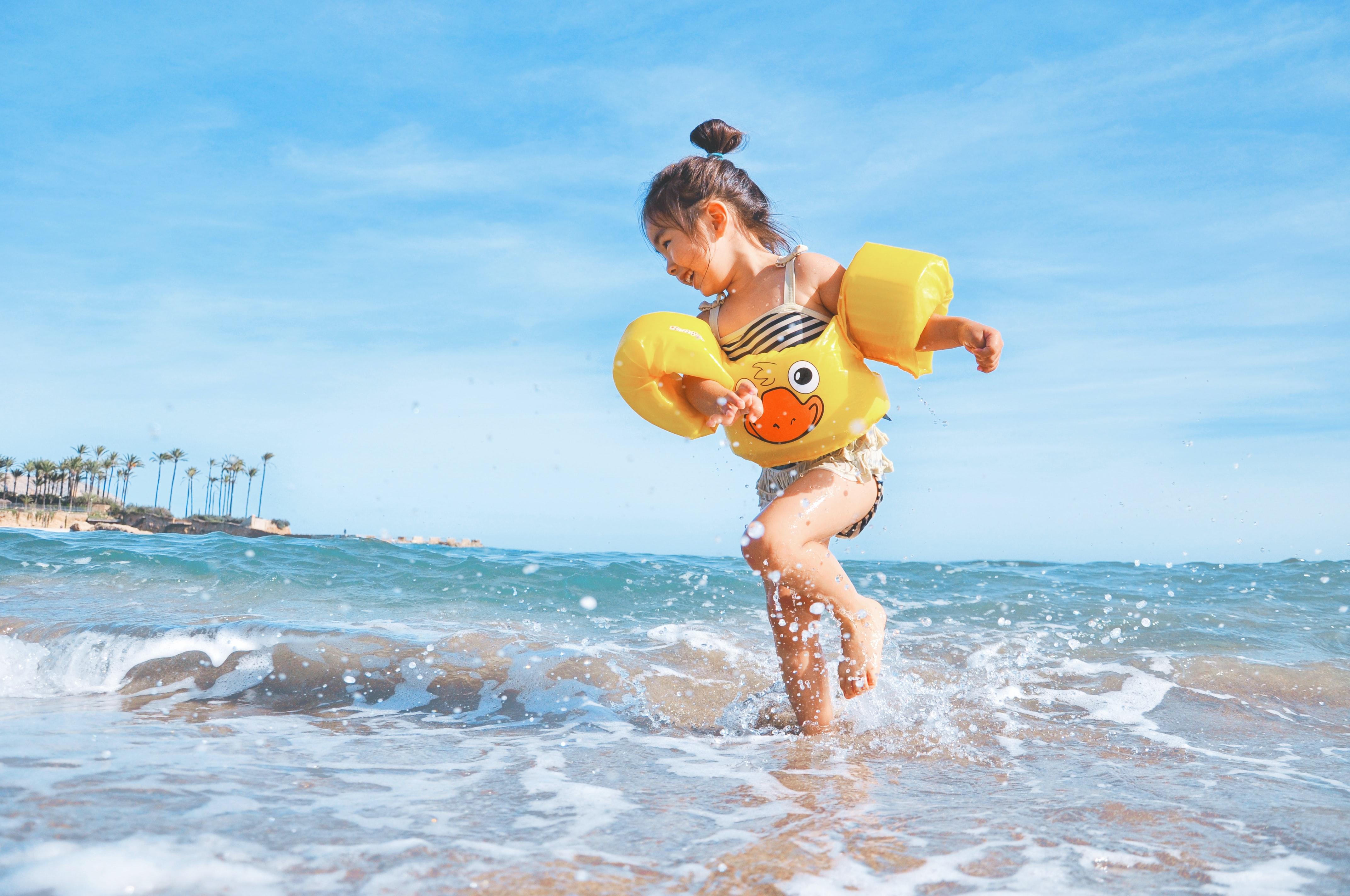 Bambina con braccioli gialli gioca con l’acqua sulla riva del mare