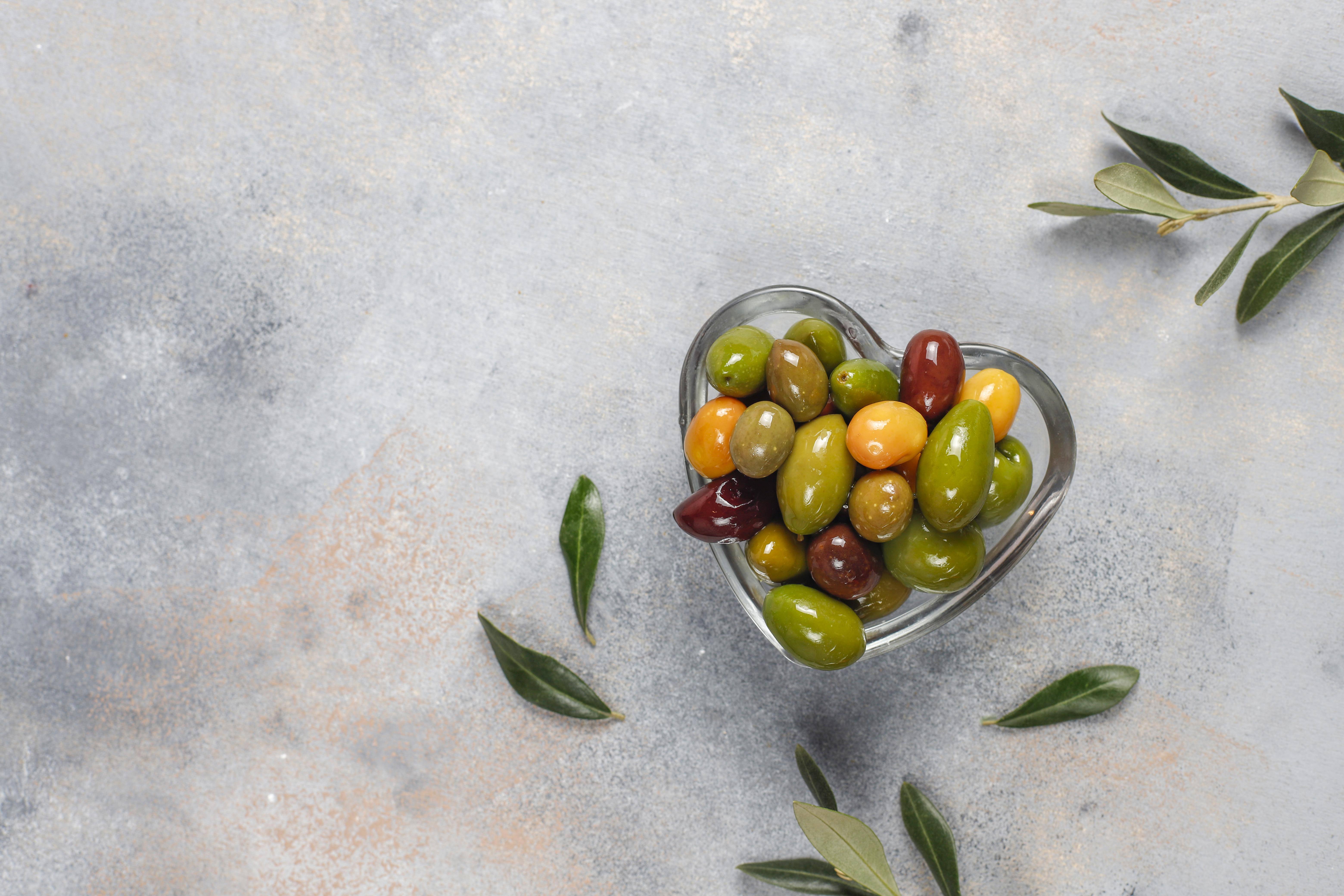 Ciotola di vetro a forma di cuore piena di olive vista dall’alto 