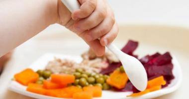 La mano di un bimbo intenzionato a mangiare il suo piatto di piselli, carote, barbabietole e pollo