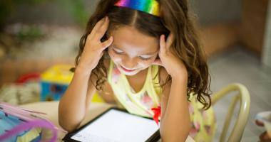 Bambina con capelli lunghi e frontino arcobaleno legge e-book nella sua cameretta