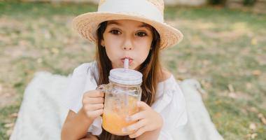 Bambina con cappello di paglia beve frullato di frutta da bicchiere di vetro