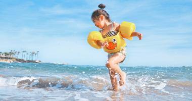 Bambina con braccioli gialli gioca con l’acqua sulla riva del mare