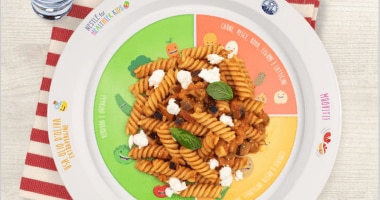 Piatto Nutripiatto con pasta alla norma visti dall’alto e bicchiere di vetro con acqua accanto