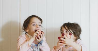 Due bambini a tavola giocano e mangiano lamponi rossi su sfondo bianco