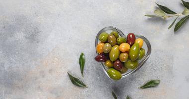 Ciotola di vetro a forma di cuore piena di olive vista dall’alto 