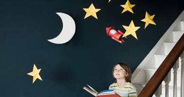 Bambino che legge un libro con sullo sfondo le stelle e la luna