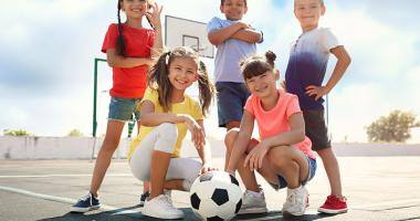 Bambini sorridenti con un pallone da calcio su un campetto da basket