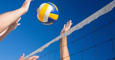 Pallone da volley sopra una rete con due persone che tentano di schiacciare la palla