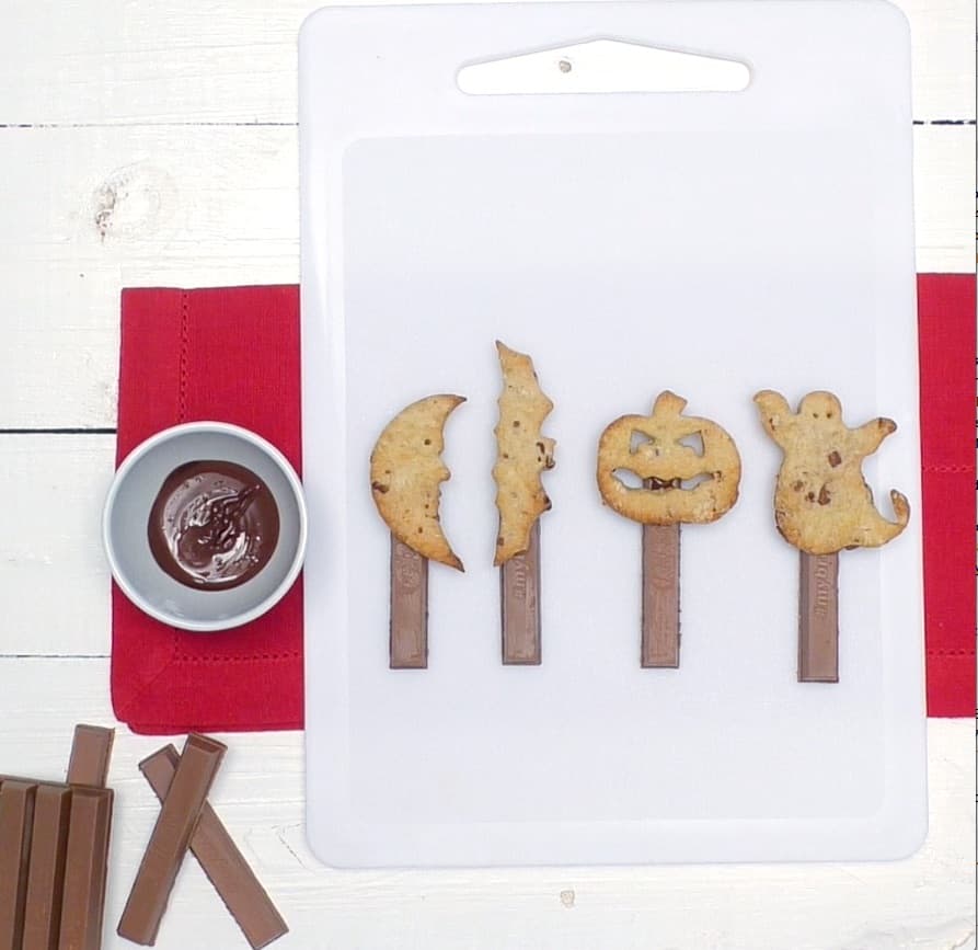 Lollipops a forma di mostri di Halloween di pasta frolla con stecco KitKat su tagliere bianco