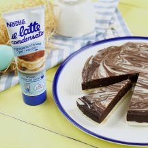 Un tubetto di latte condensato vicino ad una torta formata da uova di Pasqua al cioccolato