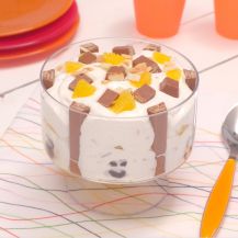 Bicchiere di vetro su tavola con KitKat Scary Cream e cucchiaio con manico giallo accanto