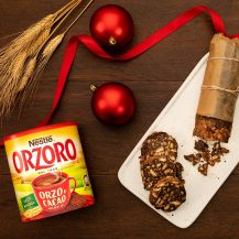 Salame di cioccolato affettato su piatto rettangolare bianco con accanto confezione di Orzoro Nestlé, nastro e palle rosse e spighe di orzo.