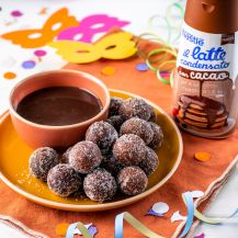 Castagnole al cacao con tazza di cioccolato, maschere di carnevale e latte condensato Nestlé al cacao accanto