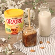 Barattolo di vetro sul tavolo con bevanda accanto confezione Orzoro e bottiglia con latte di mandorla