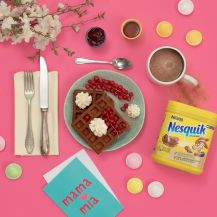 Tavola apparecchiata per la colazione con deliziosi waffle Nesquik, panna, frutta e marmellata.
