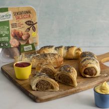 Porzioni di salsiccia in crosta vegetale su tagliere di legno e confezione Garden Gourmet accanto