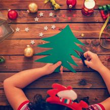 Albero di natale di cartoncino tenuto dalle mani di una bambina sopra ad un tavolo decorato natalizio