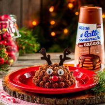 renna di pandoro su piatto con decorazioni natalizie e barattolo di latte condensato al cacao