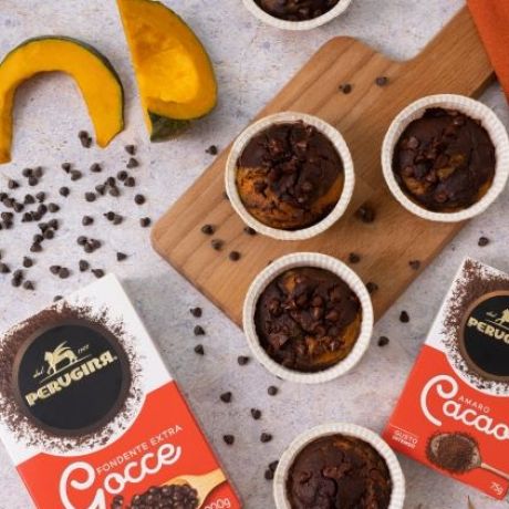 Muffin zucca e cacao su tagliere di legno tra fette di zucca e confezioni di cacao e gocce di cioccolato Perugina