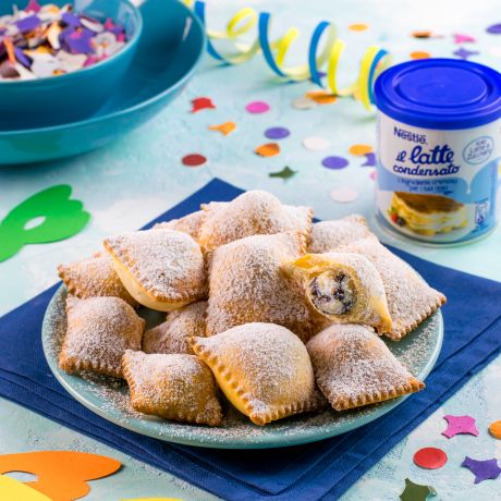 Ravioli dolci su tavola con coriandoli colorati, piatti e tovagliolo blu con confezione di latte condensato Nestlè accanto 