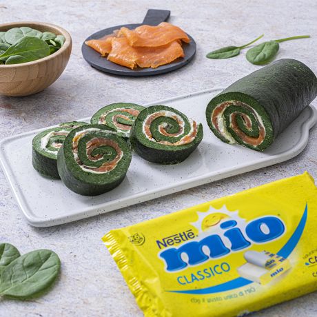 Rotolo di spinaci su piatto bianco con accanto ingredienti e confezione di formaggino Mio