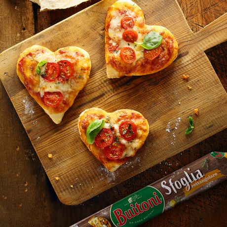 Pizzette a cuore su tagliere di legno e sfoglia Buitoni accanto