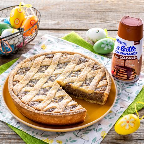 Pastiera al cacao con gocce di cioccolato bianco in tavola e confezione di latte condensato al cacao Nestlé accanto