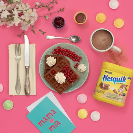Tavola apparecchiata per la colazione con deliziosi waffle Nesquik, panna, frutta e marmellata.