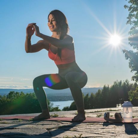 Giovane donna che fa squat al parco su tappetino