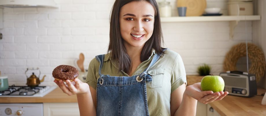 Ragazza in cucina con una mela e un dolce in mano