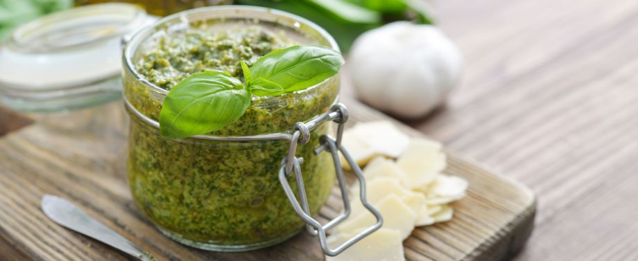 pesto in barattolo di vetro su tavola di legno con foglia di basilico sopra e scaglie di parmigiano accanto