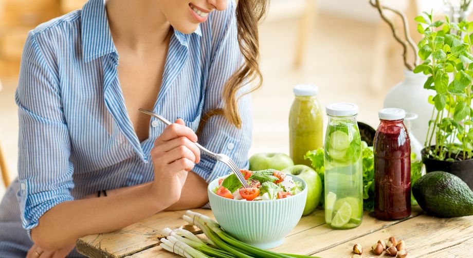 Ragazza a tavola con piatto di insalata, verdure, frutta e succhi