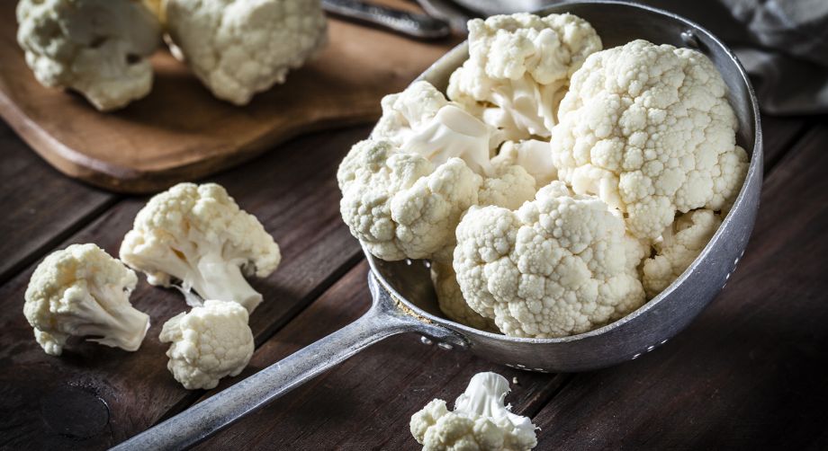 Cavolfiore tagliato a pezzi in un vecchio colapasta di alluminio su tavola di legno