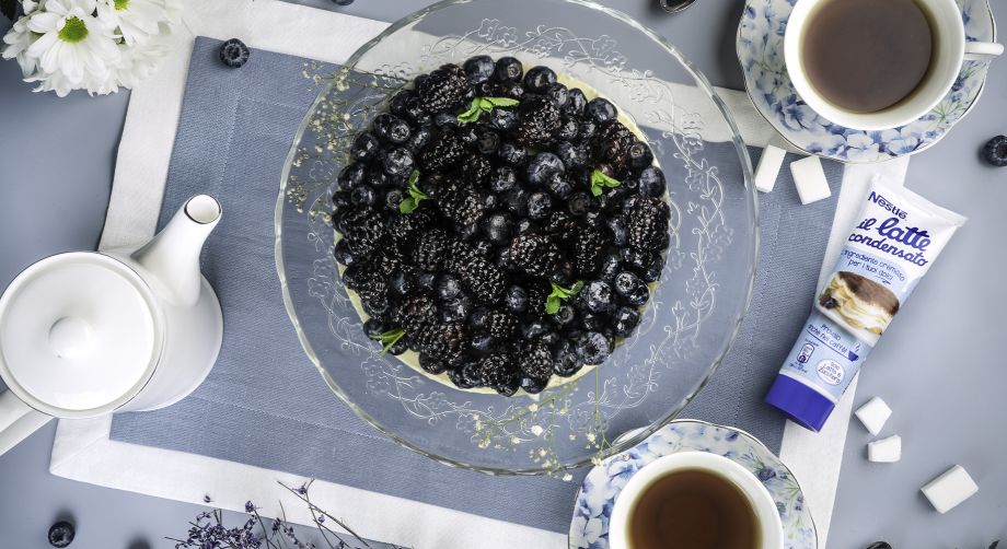 Tavola vista dall’alto con cheesecake ai frutti di bosco, tazzine di caffè e confezione di latte condensato Nestlè