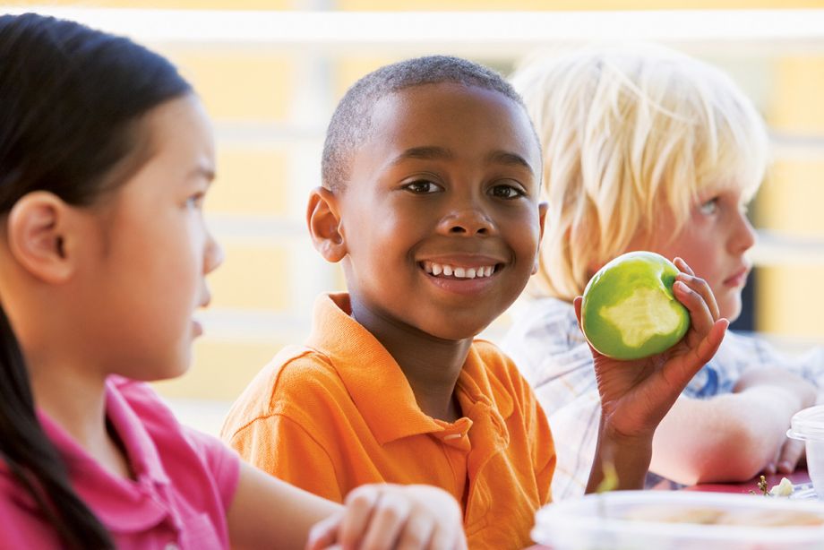 Bambino di colore con mela in mano sorride con accanto bambina asiatica e bambino biondo